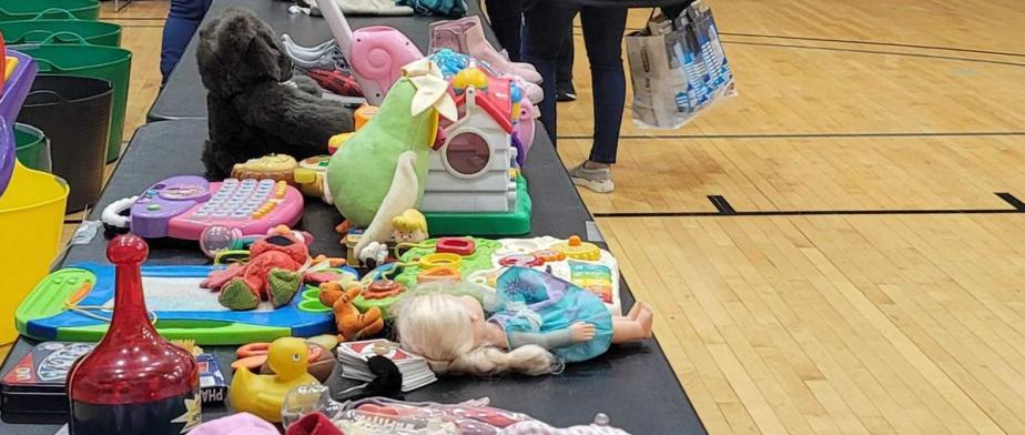 2 people standing next to tables with children clothing and toys